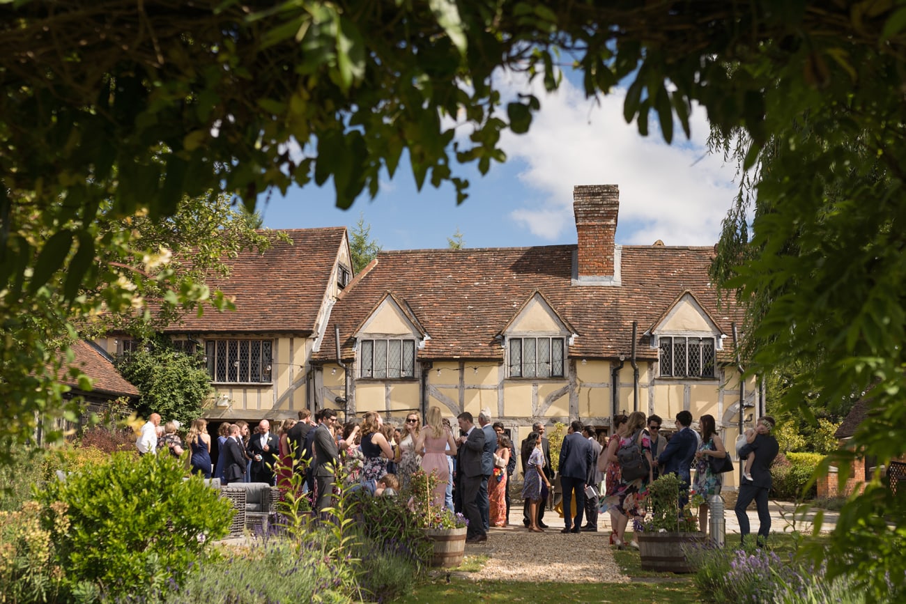 The courtyard at Cain Manor full of wedding guests enjoying the drinks reception. The photos is framed by foliage