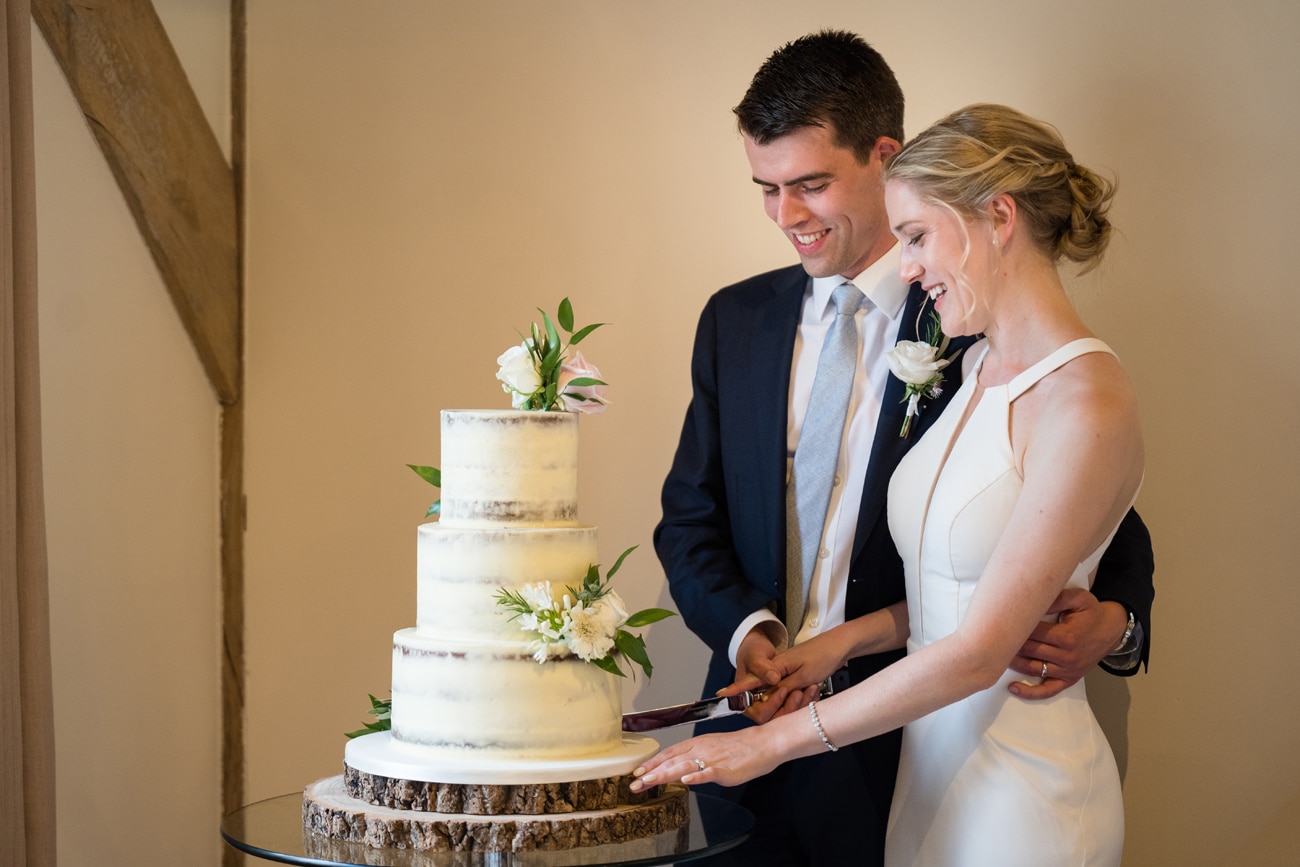 The bride and groom cutting a semi-naked wedding cake decorated with white and pink fresh flowers