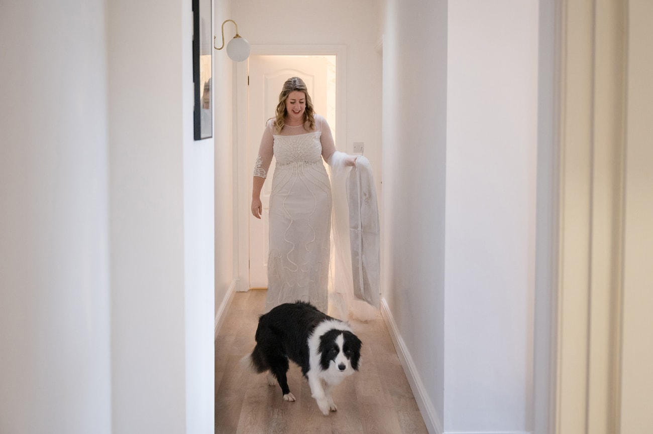 Bride walking down the hall with her dog after putting on her wedding dress