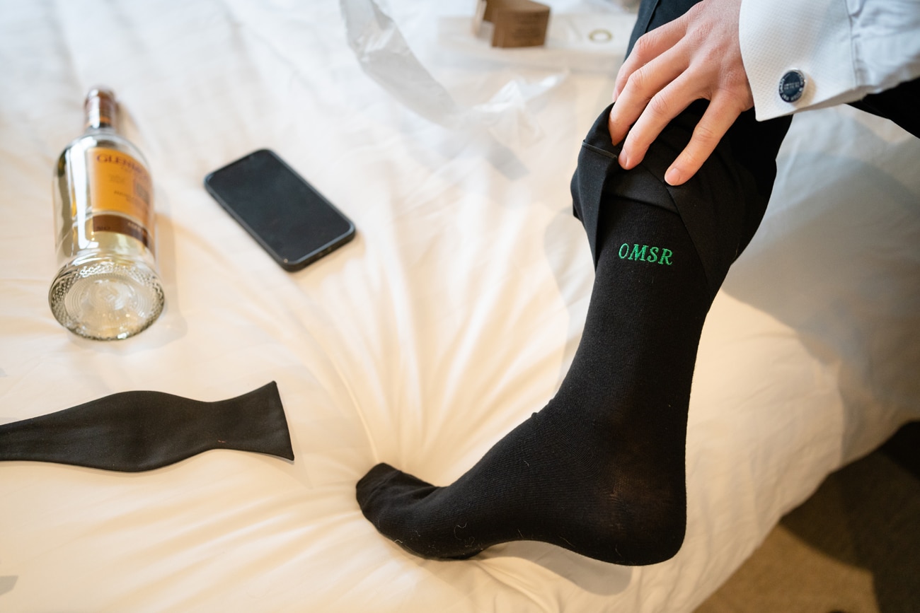 A close-up photo of the groom's black socks personalised with his initials in green stitching