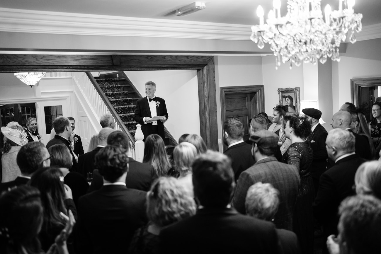 Father of the bride making a speech from a staircase with the guests gathered below at Plum Park Manor