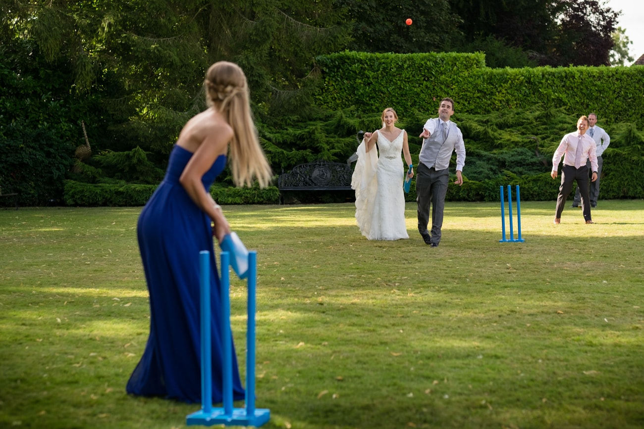 Groom bowling a cricket ball to a bridesmaid on the lawn at Plum Park Manor