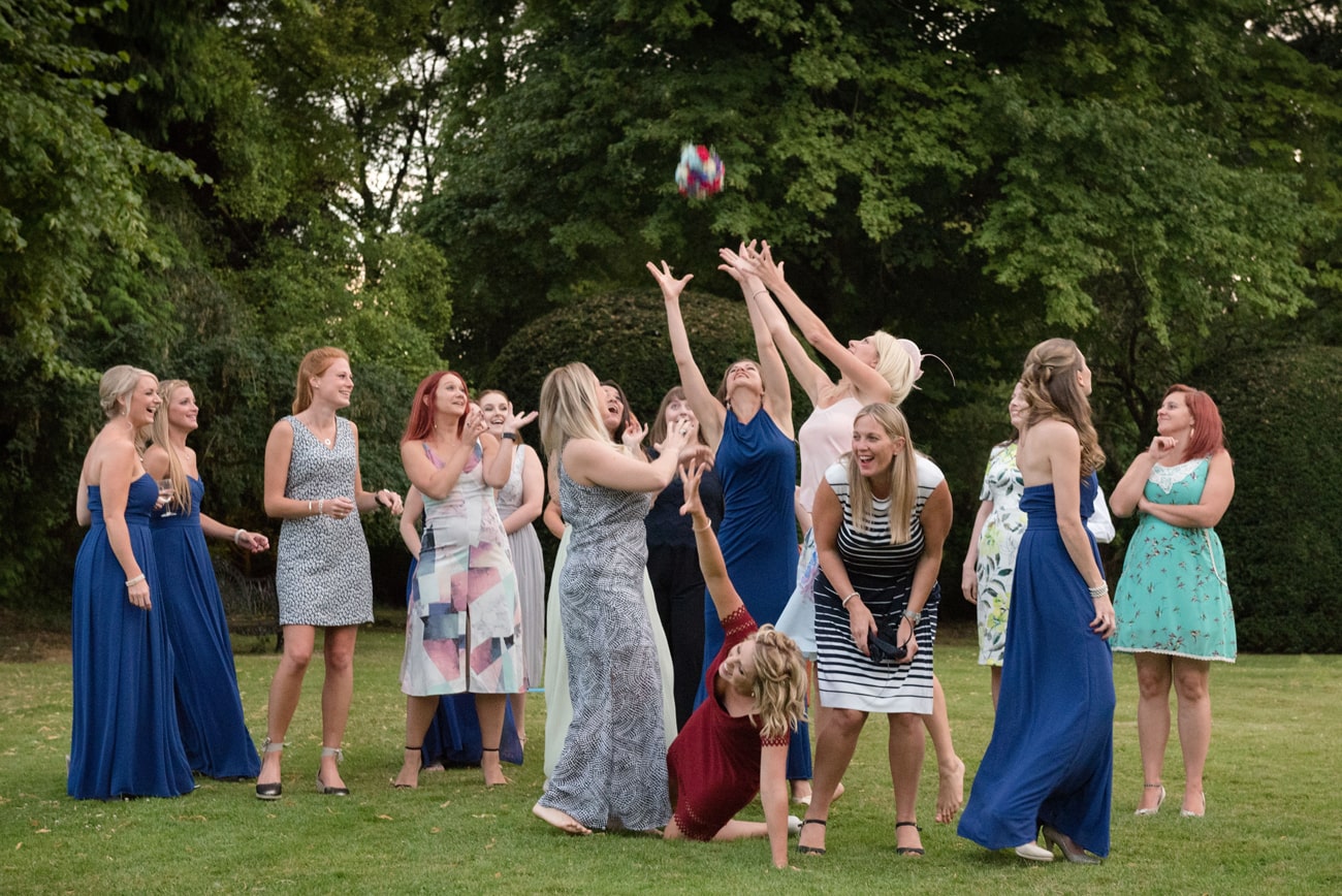 Female wedding guests reaching to catch the bride's bouquet toss in the garden at Plum Park Manor