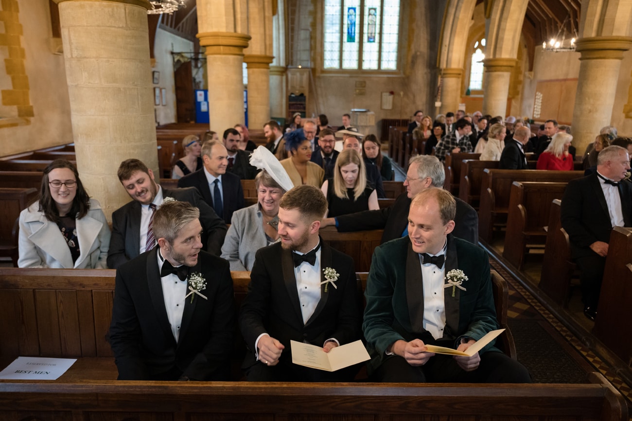 Groom and his best men sitting in a pew waiting for the bride to arrive at St Michael's church in Silverstone