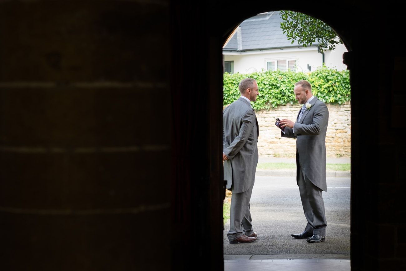 Two groomsmen waiting to welcome wedding guests at St Peter's church in Weston Favell