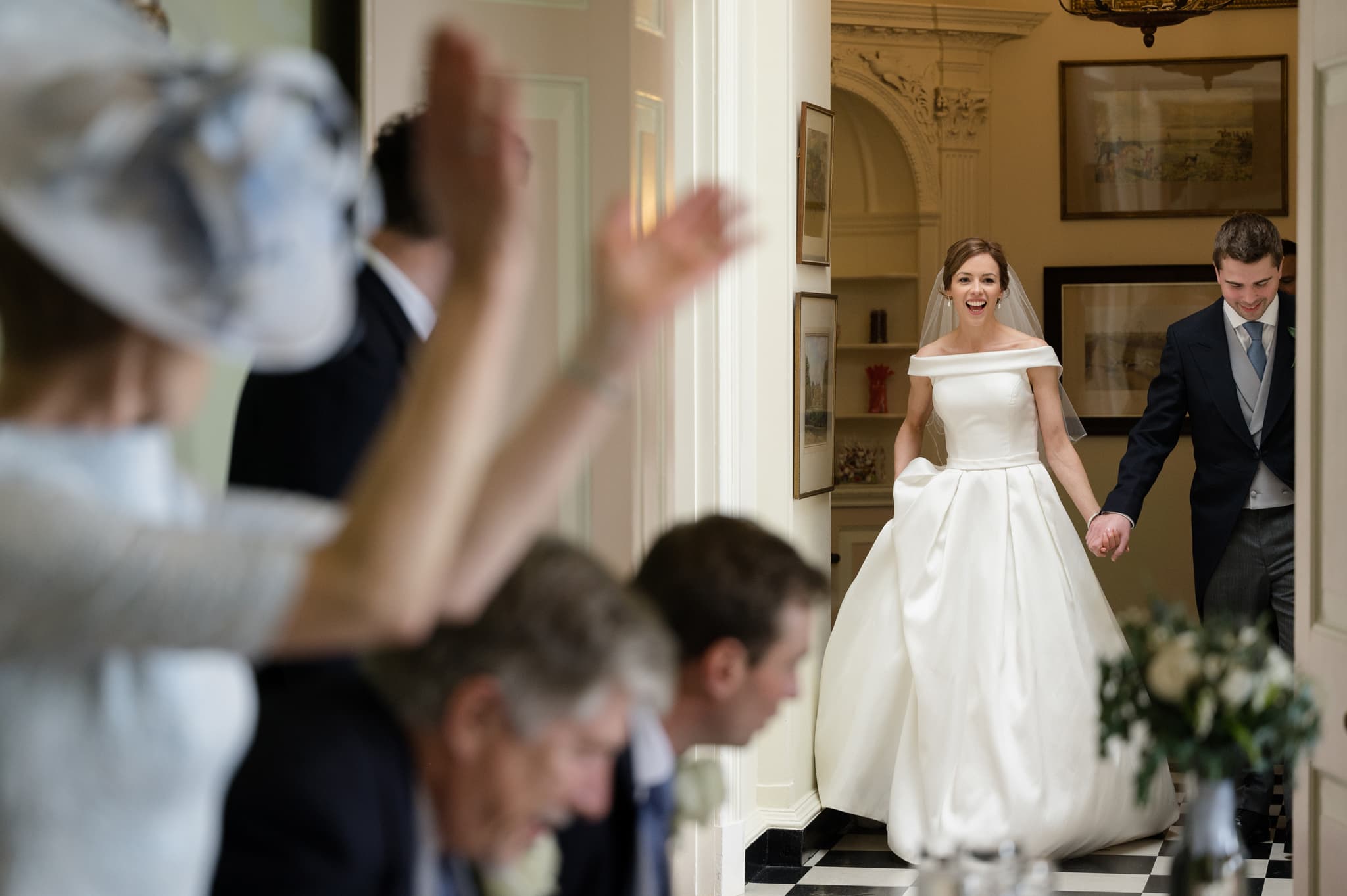 Bride and groom entering room for dinner with one of their guests clapping in the foreground