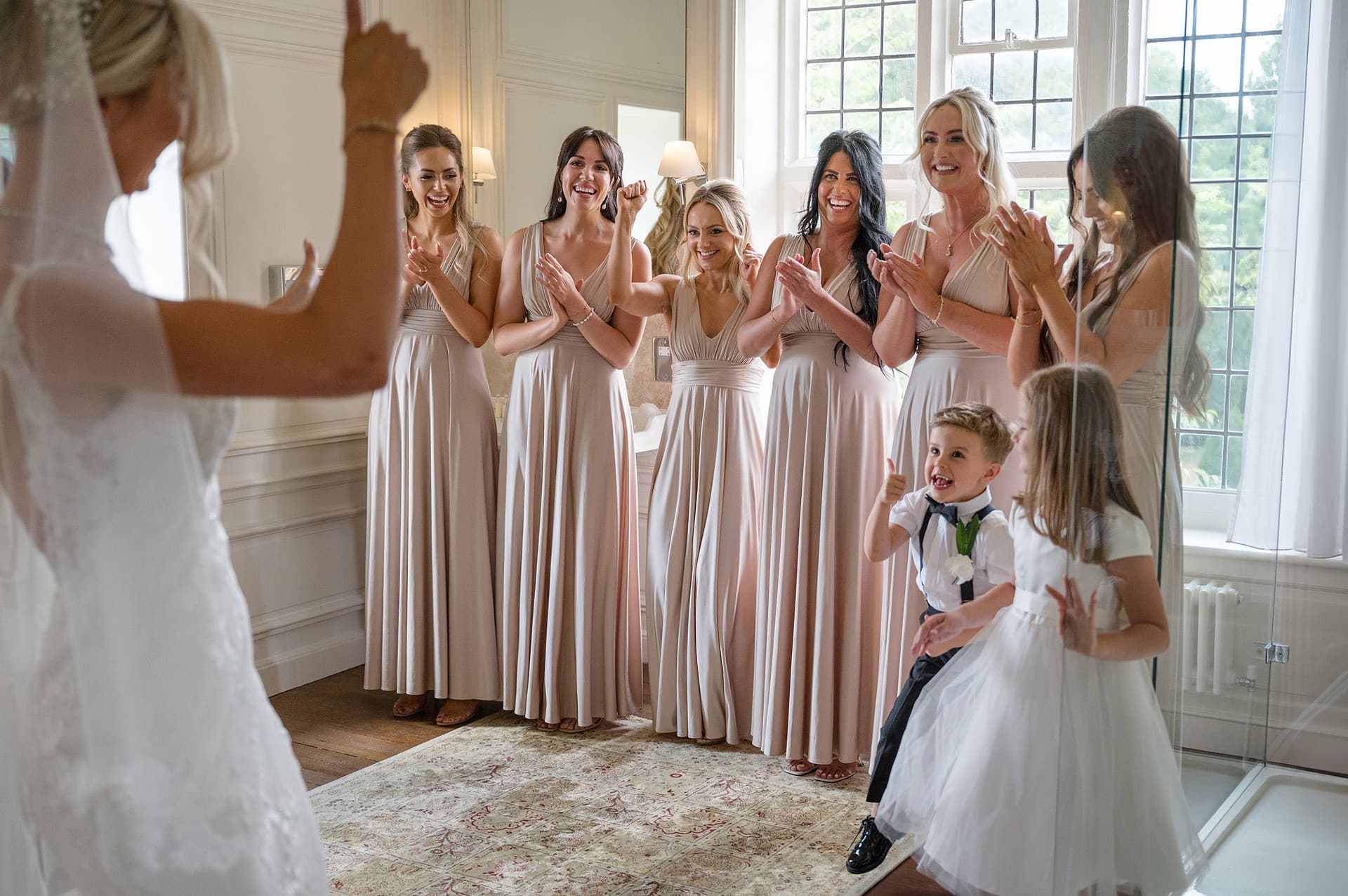 Bridesmaids' reaction to seeing bride in her dress with pageboy giving a thumbs up