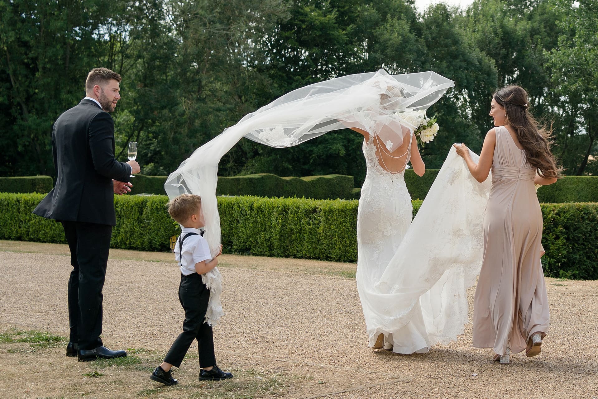Pageboy getting covered in bride's veil as it blows in the wind