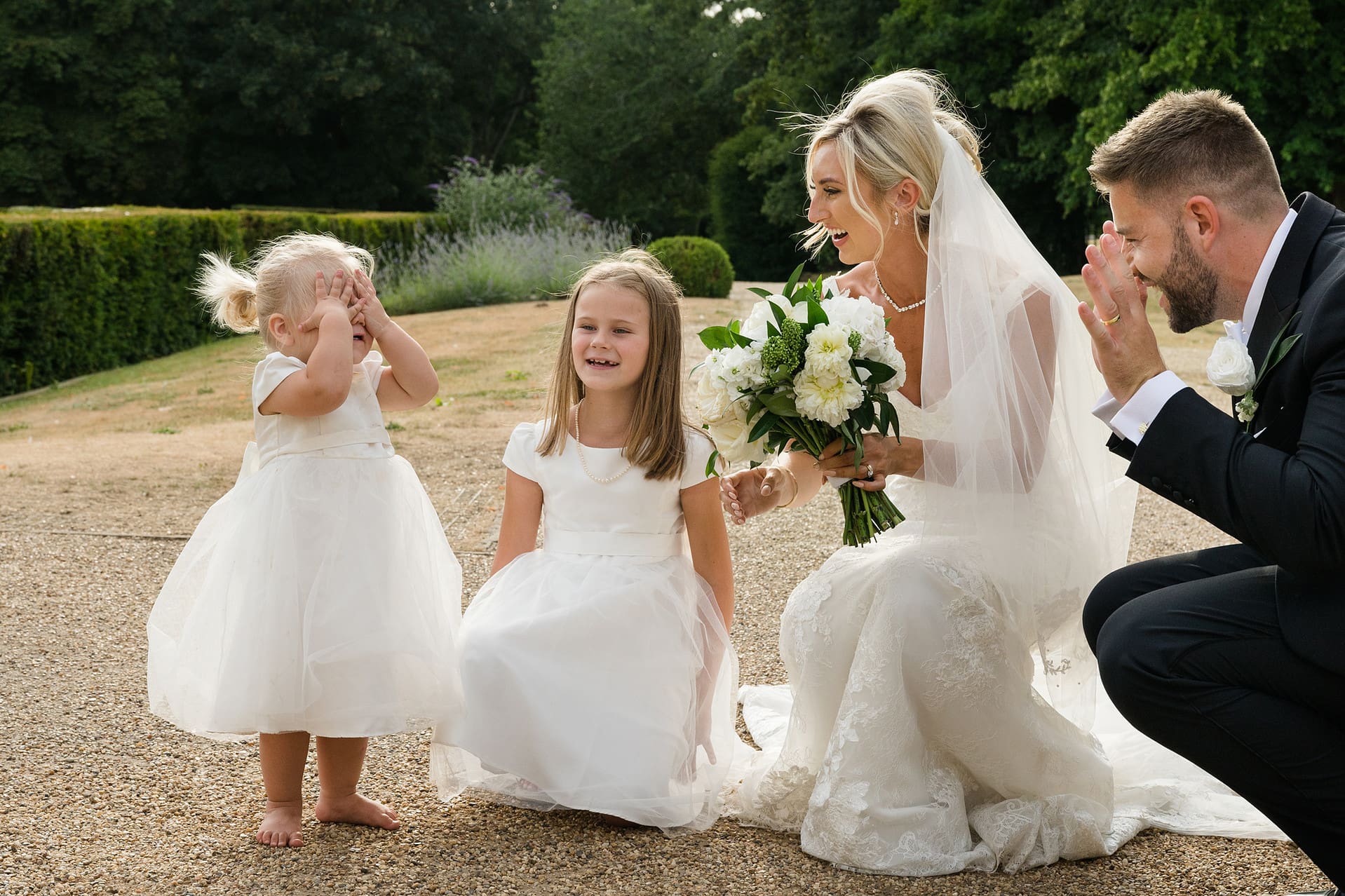 Bride and groom playing peekaboo with a young flower girl