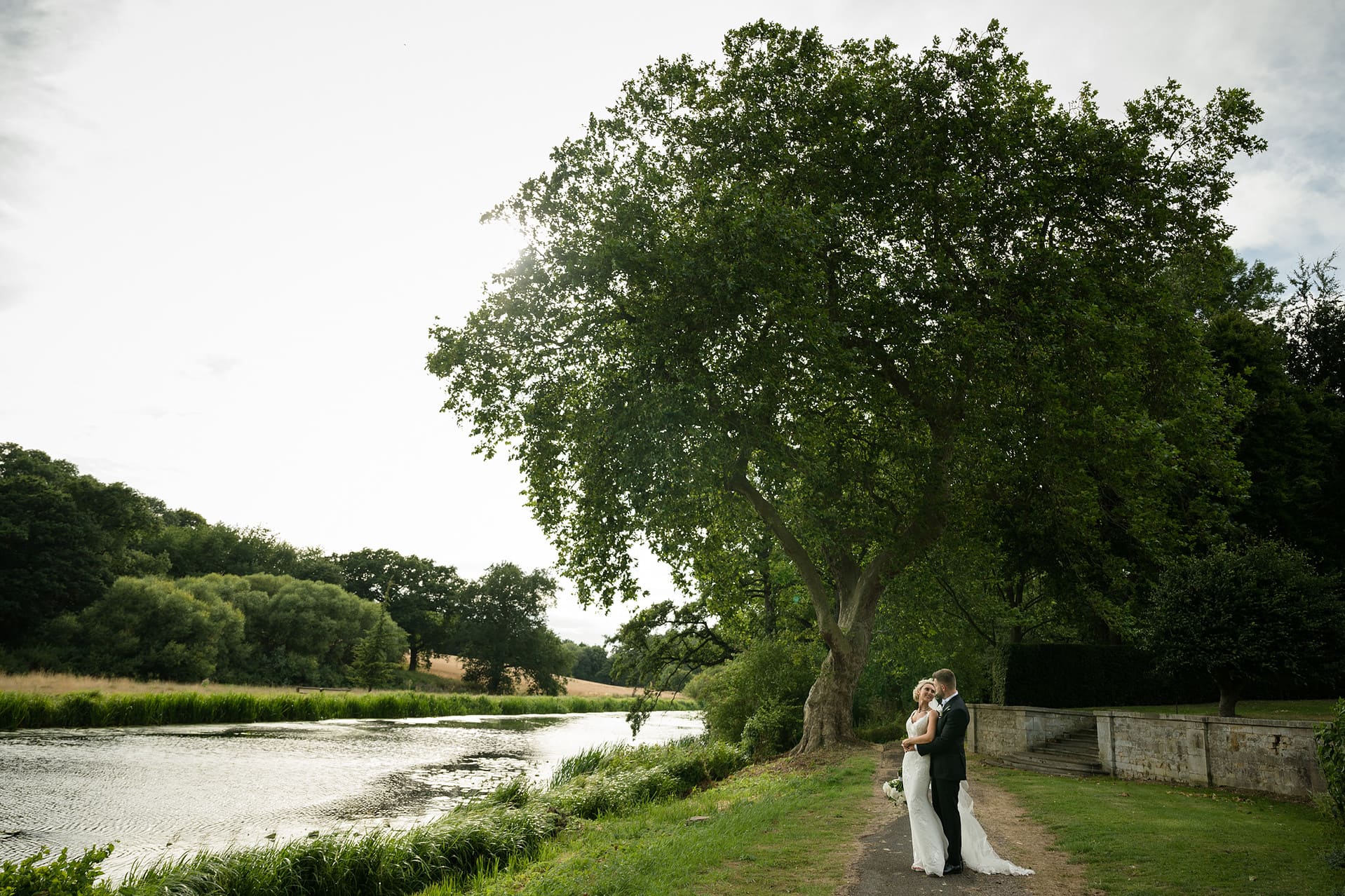 Bride and groom standing together in front of a large tree by a lake
