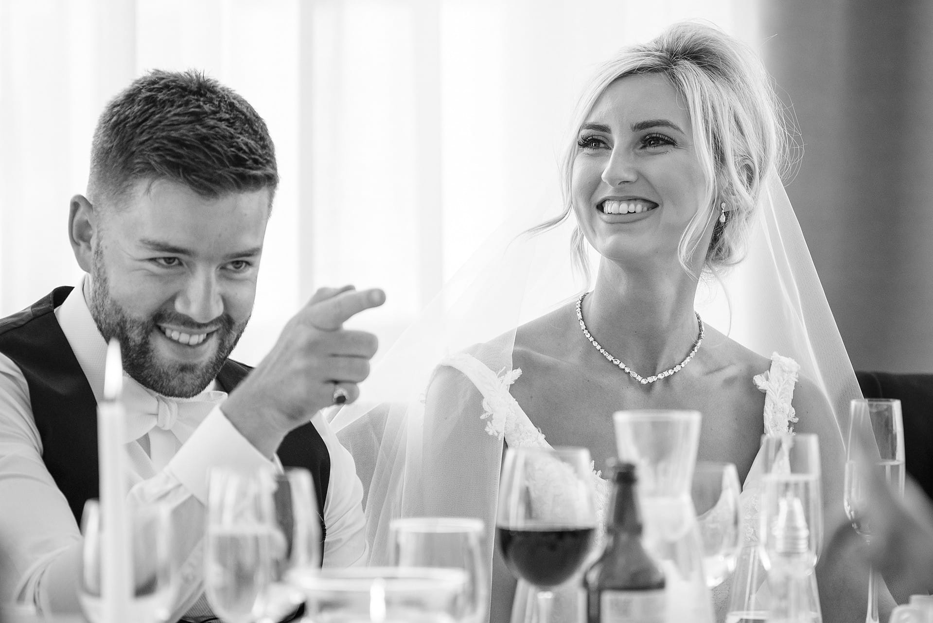 Bride smiling and groom pointing knowingly at a guest during speeches