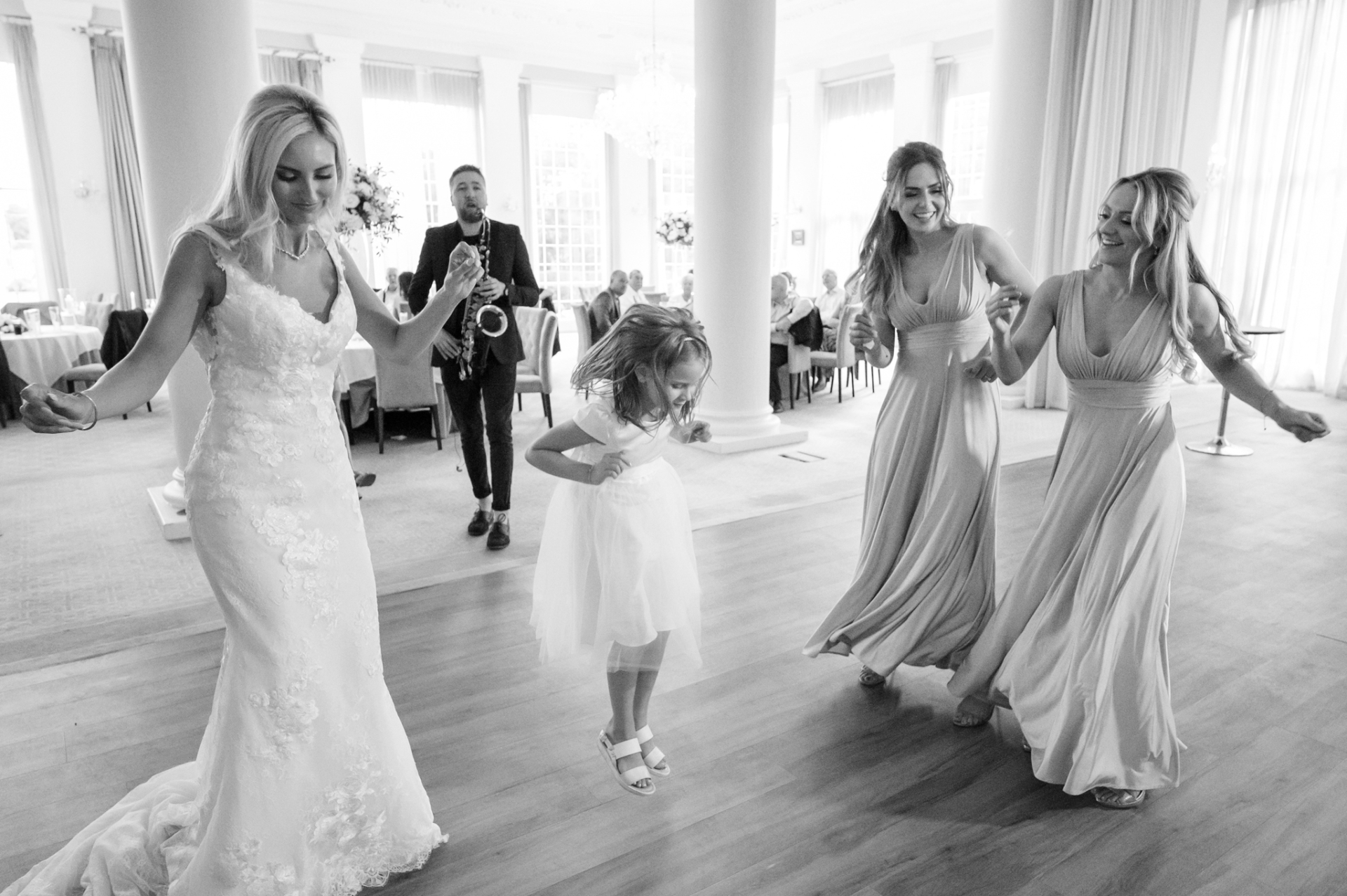 Flower girl jumping in the air as she dances with adult bridesmaids