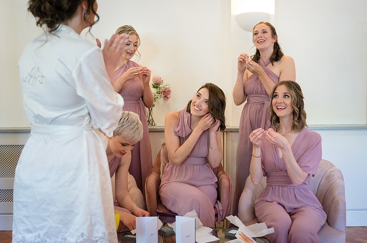 Bridesmaids sitting in a group and putting on earrings which they've just received as a wedding gift from the bride