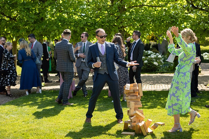 Wedding guests raising their hands in delight as the giant jenga falls to the ground