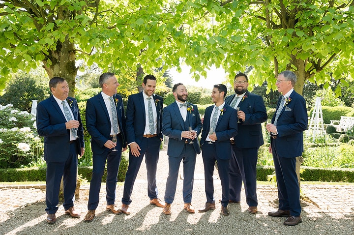 Casual group photo of groomsmen chatting and laughing with drinks in their hands