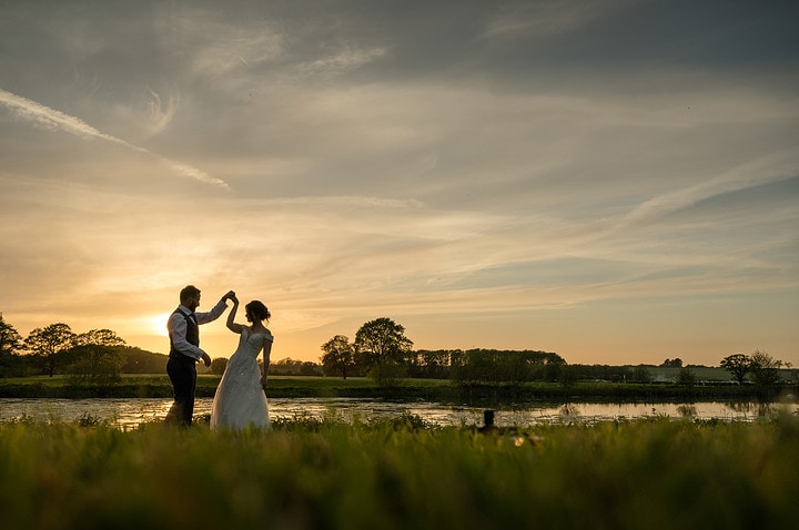 Bride and groom dancing by the lake at Kelmarsh Hall at sunset
