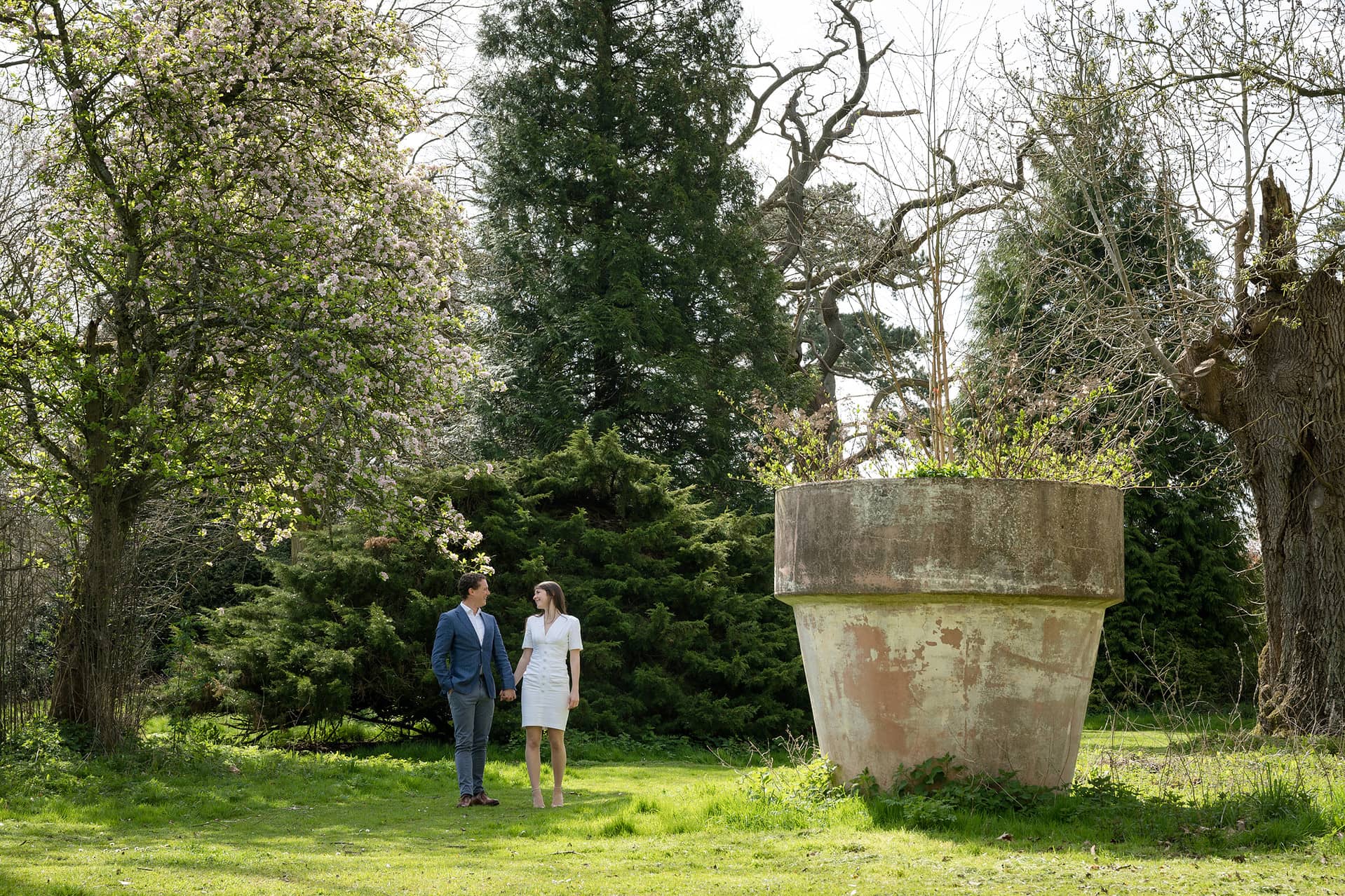 Engaged couple walking past a giant flower pot in the grounds of Courteenhall