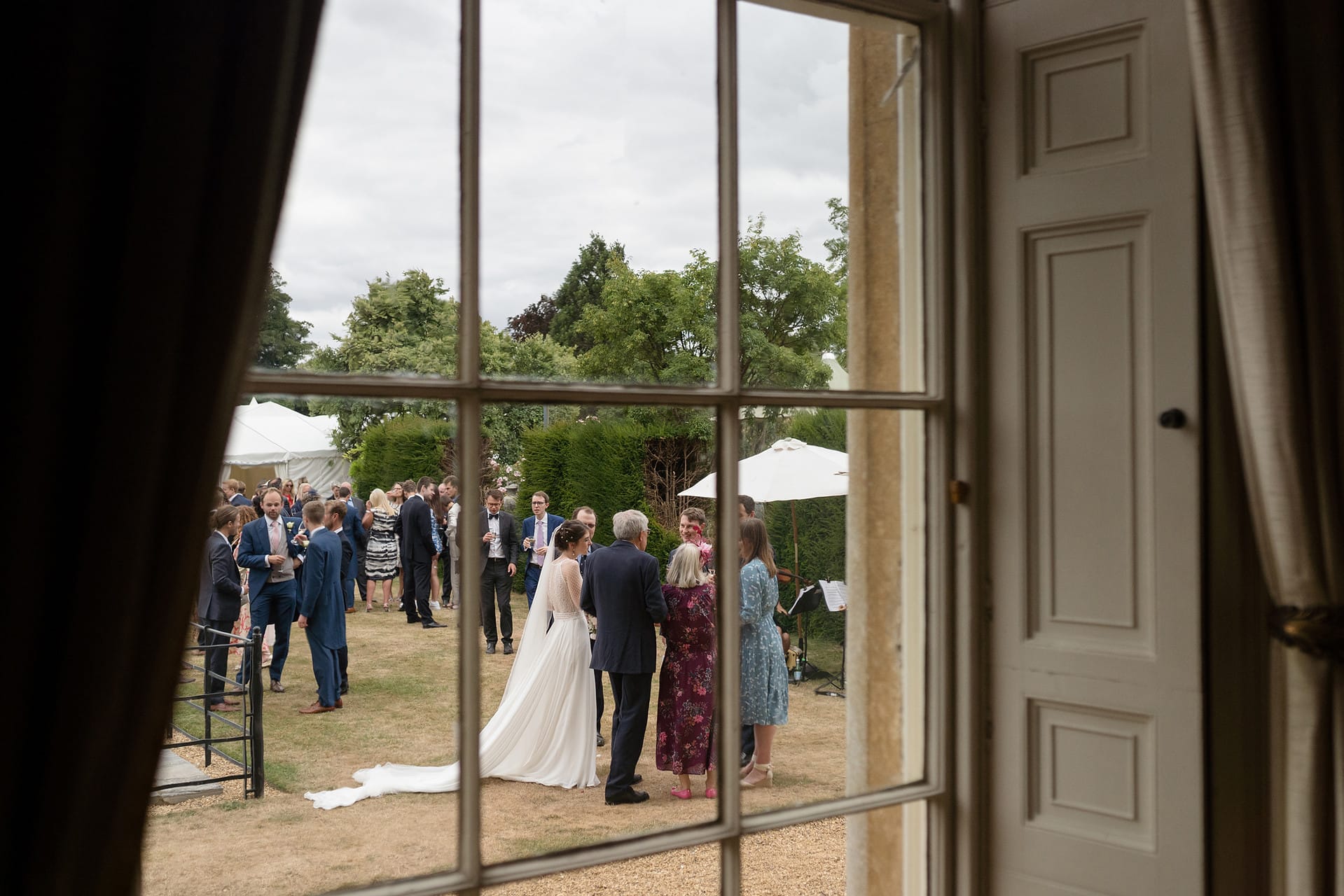 A view through a period sash window of a wedding drinks reception on a lawn