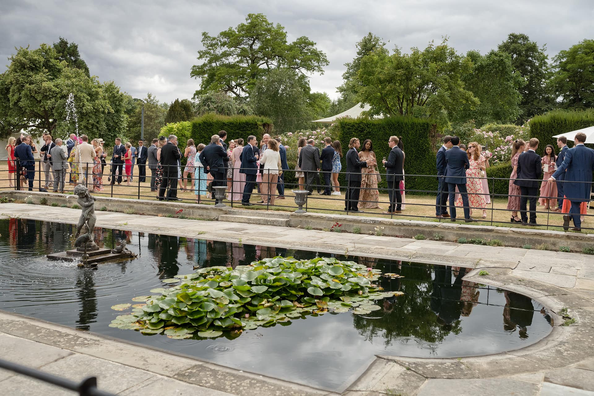 View of a wedding drinks reception across the lily pond at Courteenhall