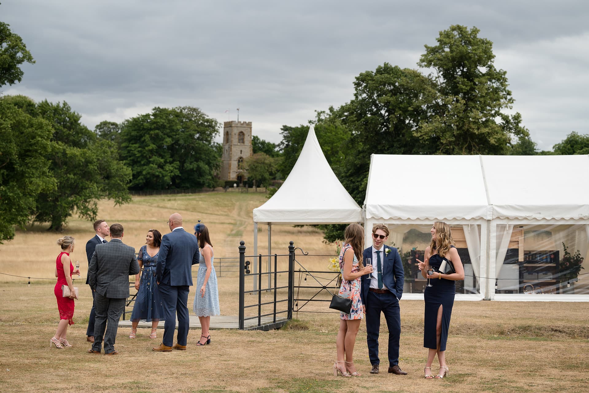 Guests chatting outside a wedding marquee with the church in the background