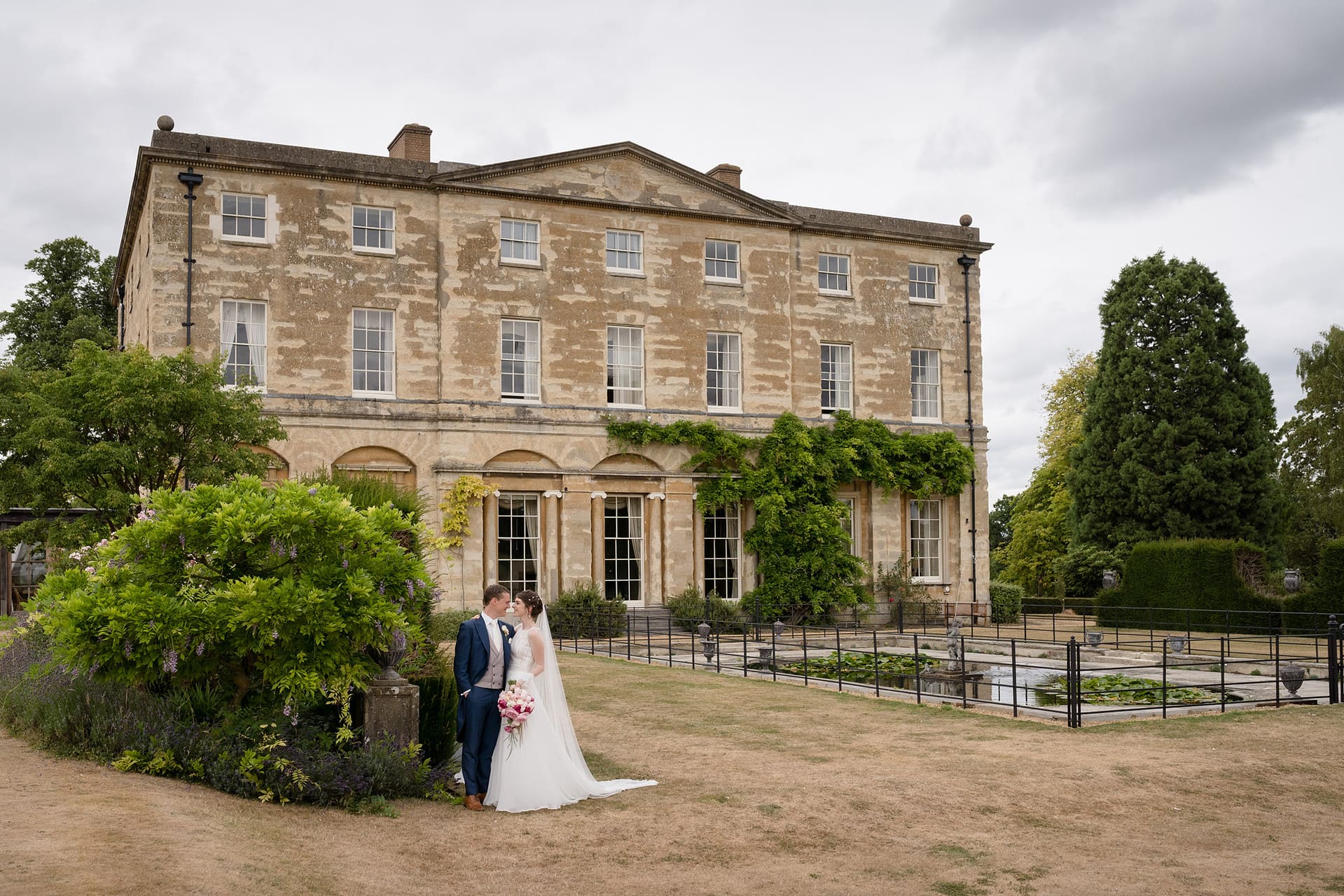 Bride and groom posing for a photo with Courteenhall house behind them