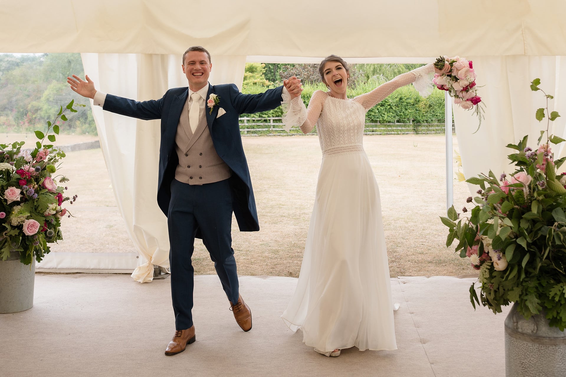 Bride and groom walking into their marquee for the wedding breakfast with their arms outstretched