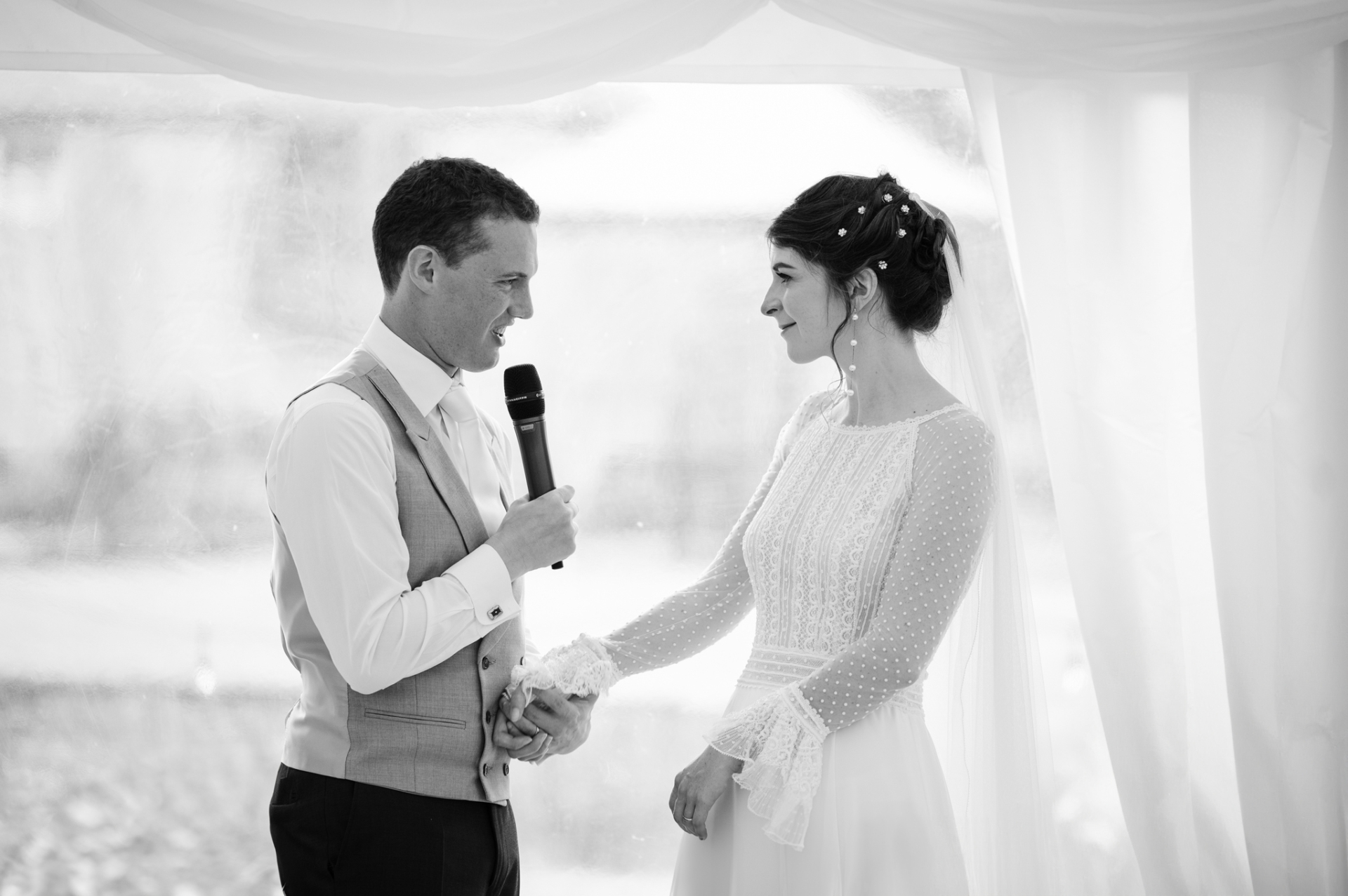Groom holding the bride's hand as he speaks directly to her during their joint speech