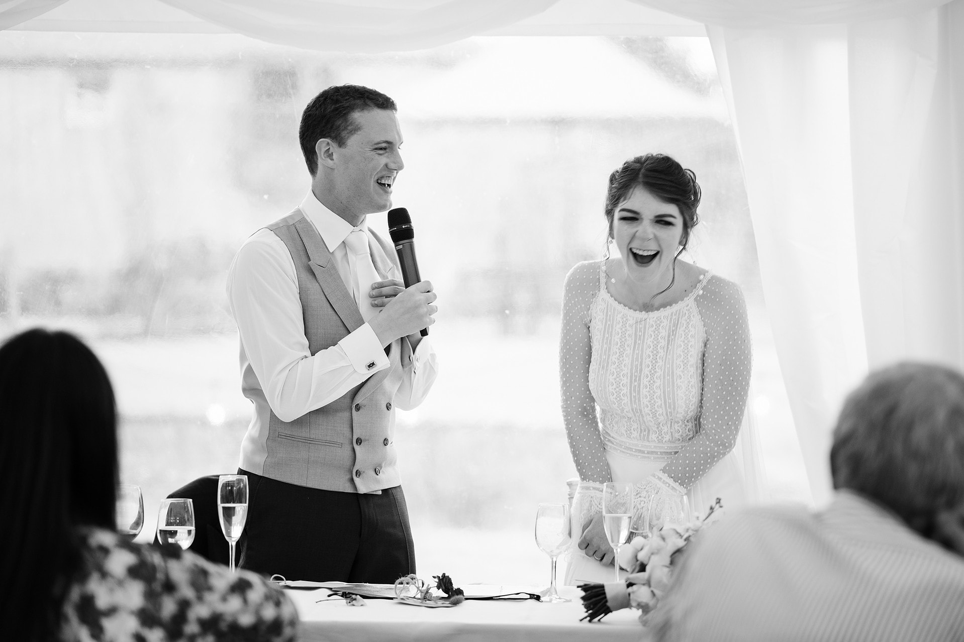 Bride laughing as the groom speaks about her during their joint speech