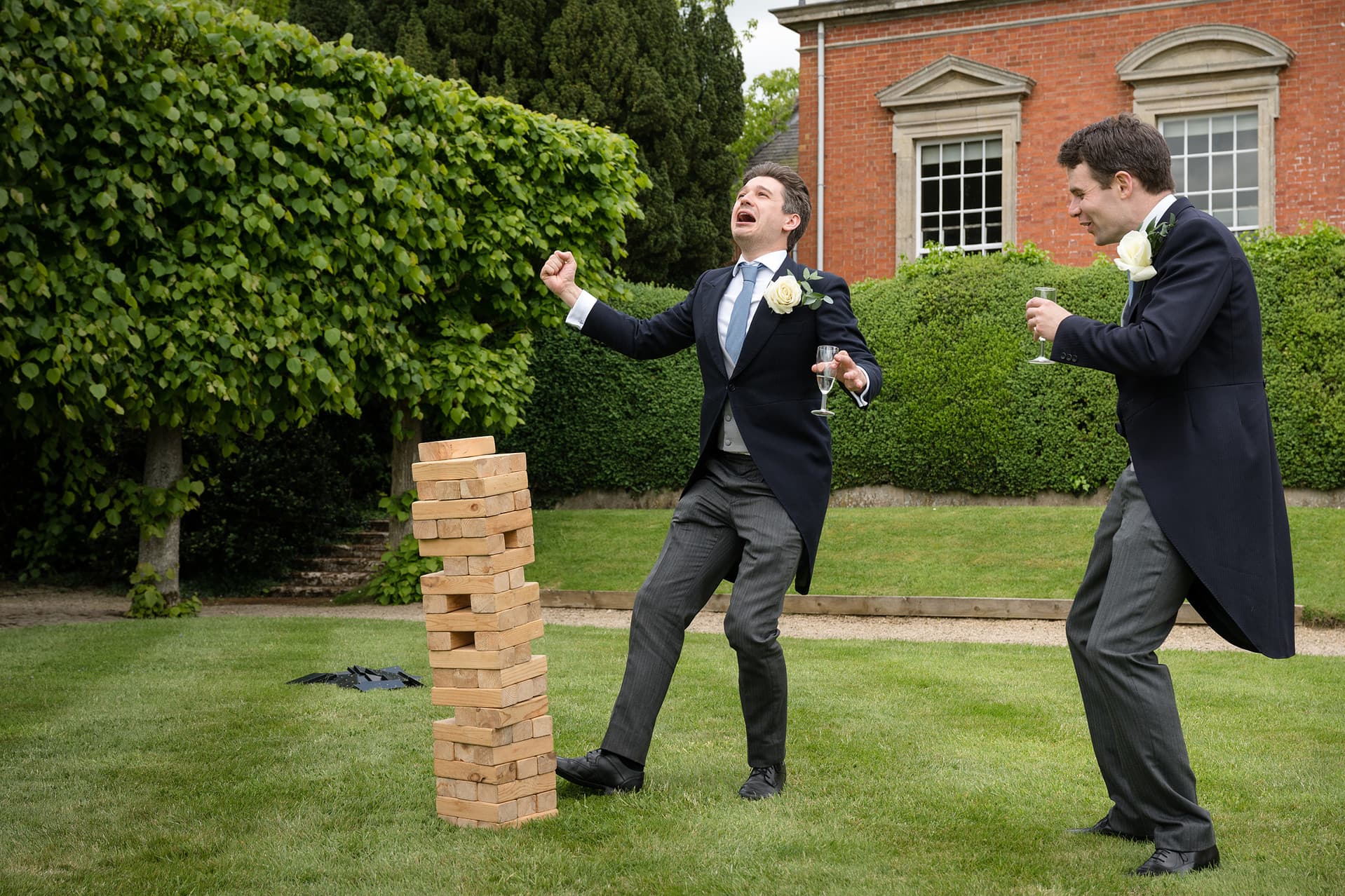 Two ushers in tails making funny faces as they play a game of giant jenga