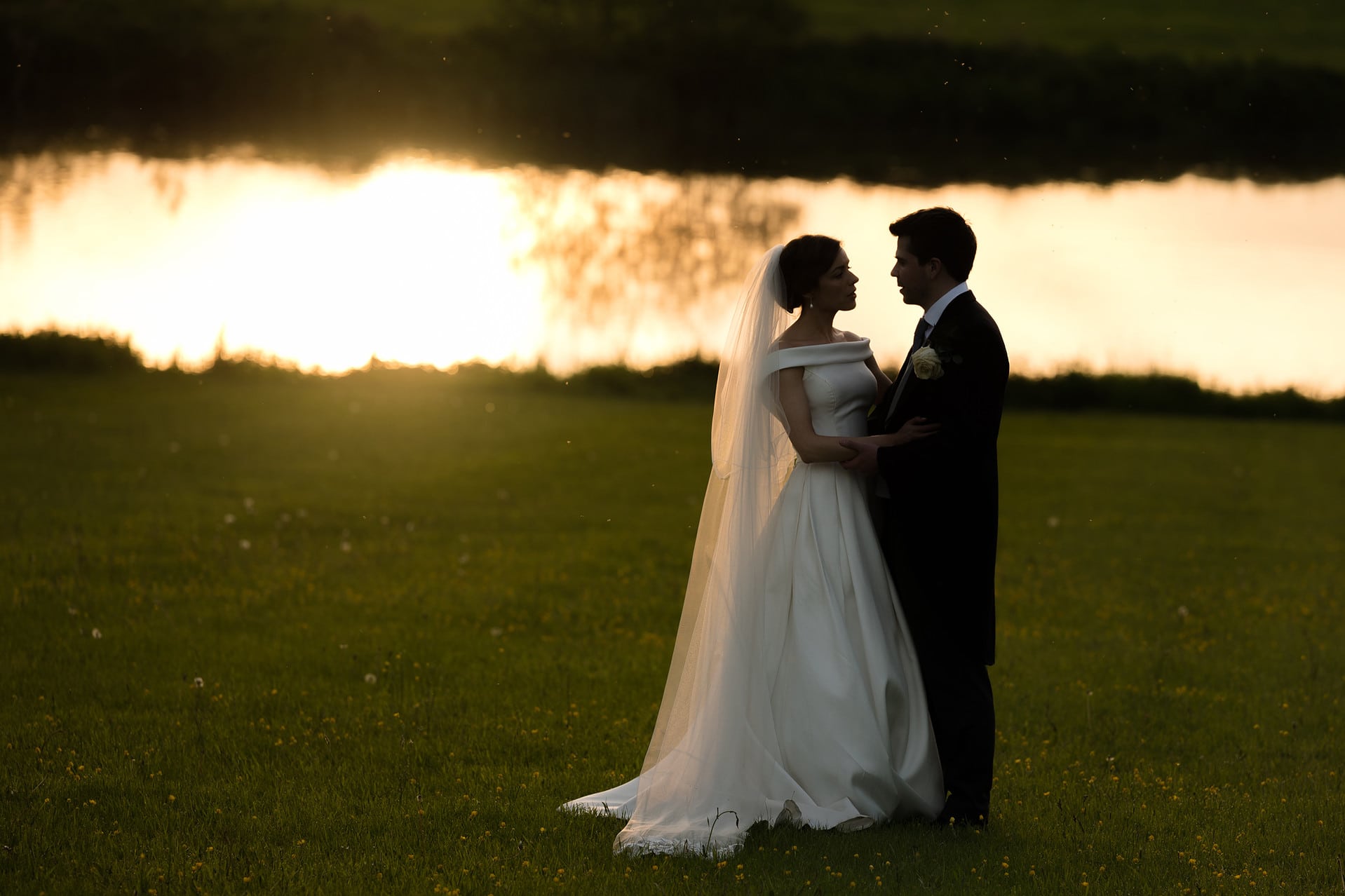 A semi-silhouette of the bride and groom during golden hour by the lake at Kelmarsh Hall