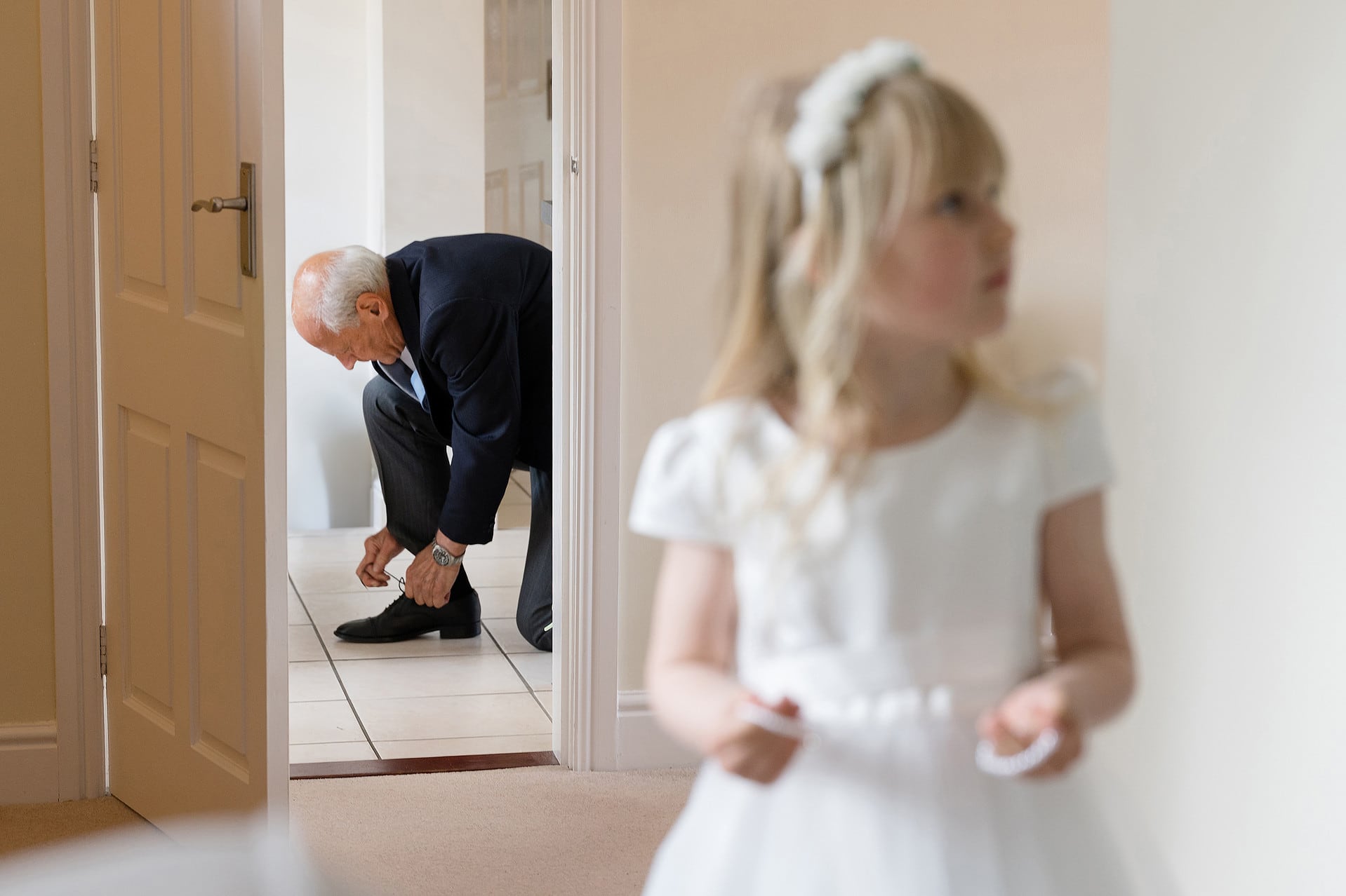 Bride's dad bending down to tie his shoelace with flower girl out of focus in the foreground