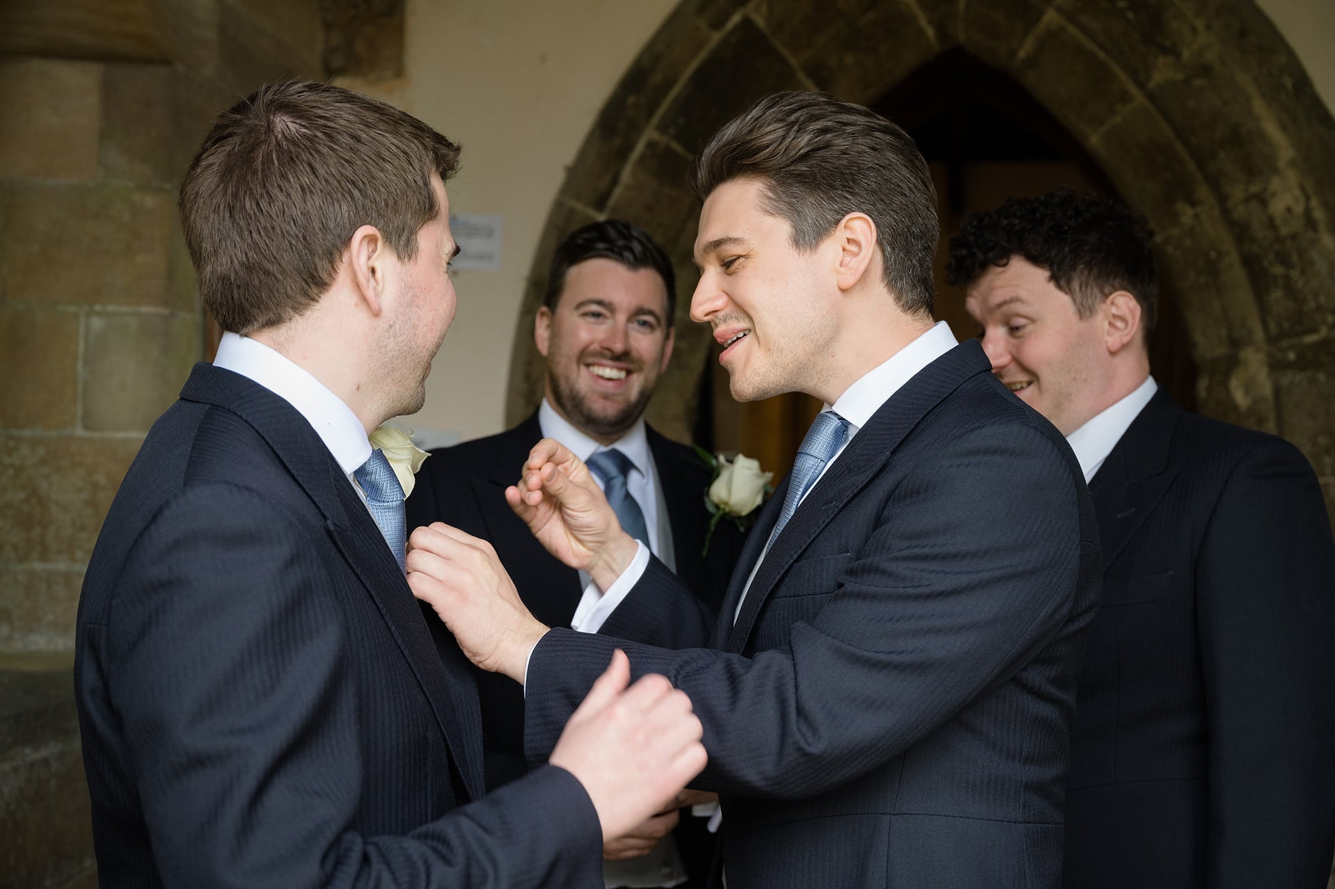 Groomsmen laughing as they try to pin on the groom's buttonhole