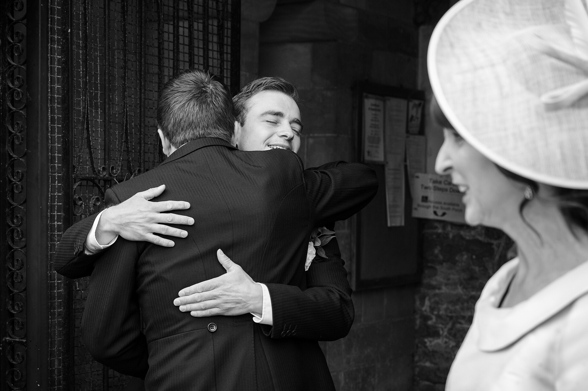 The groom hugging a wedding guest in the church porch