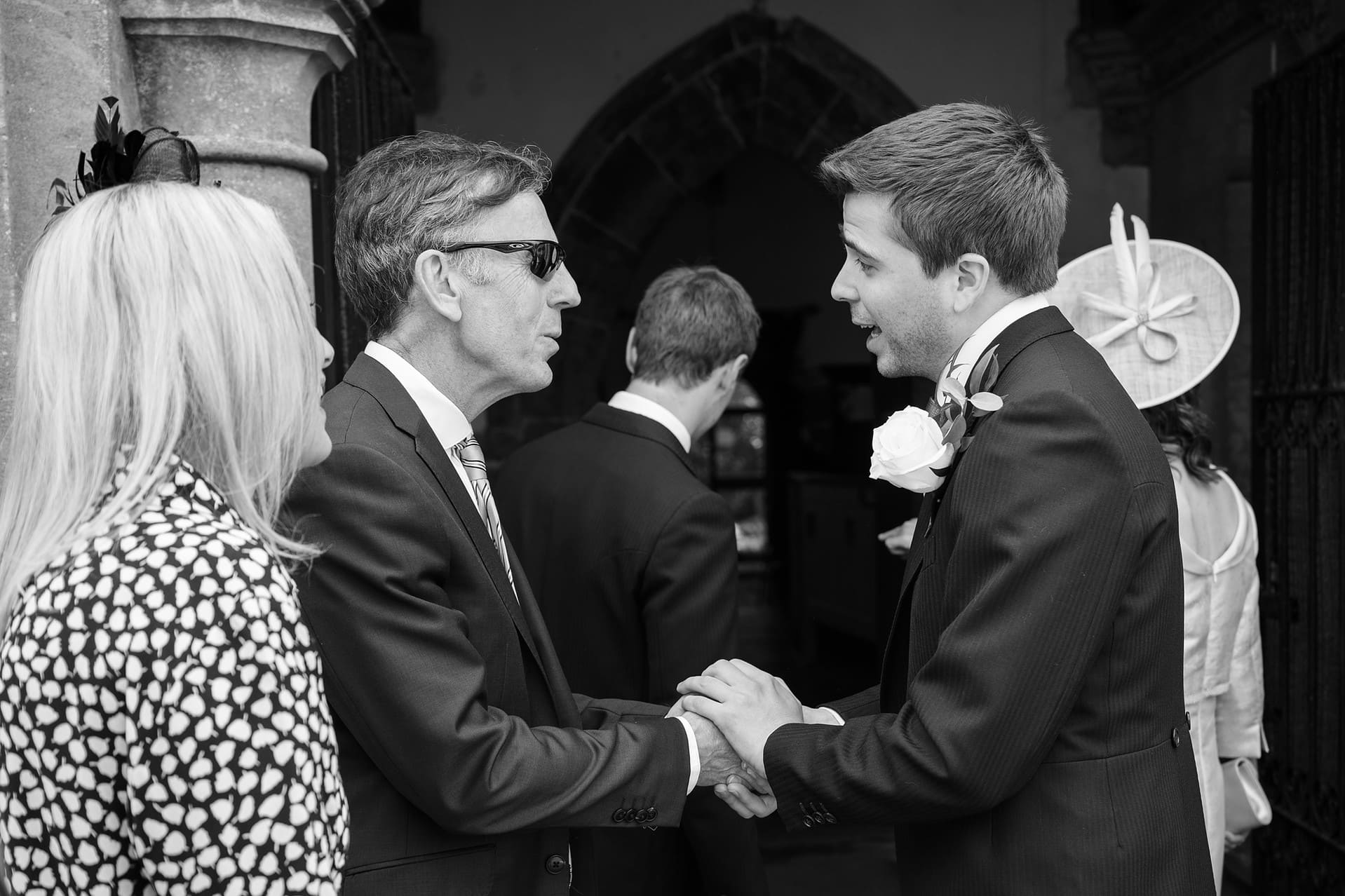 The groom holding hands with a wedding guest as they greet each other