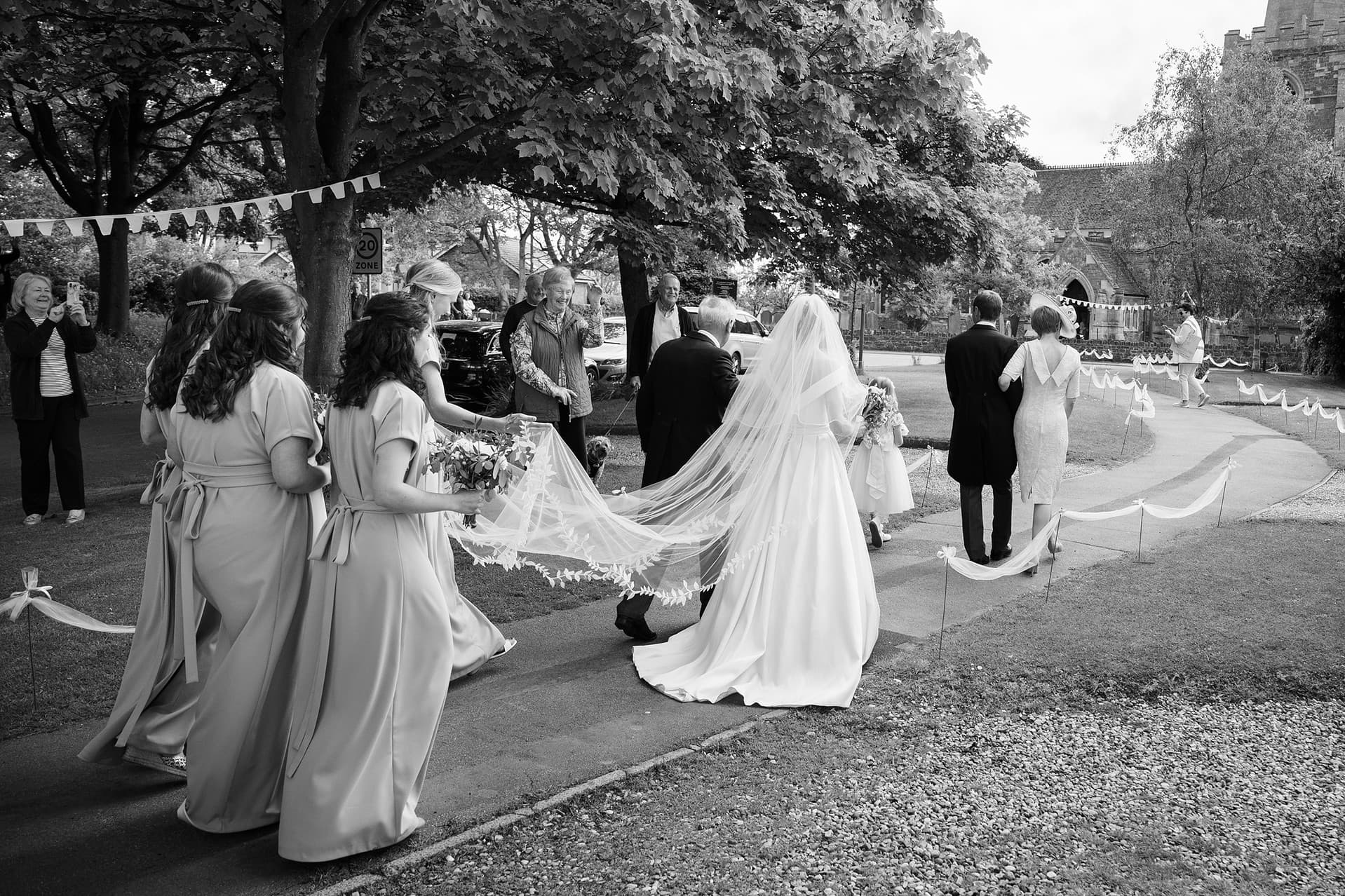 The bride and her entourage walking towards St Catharine's church in Houghton on the Hill