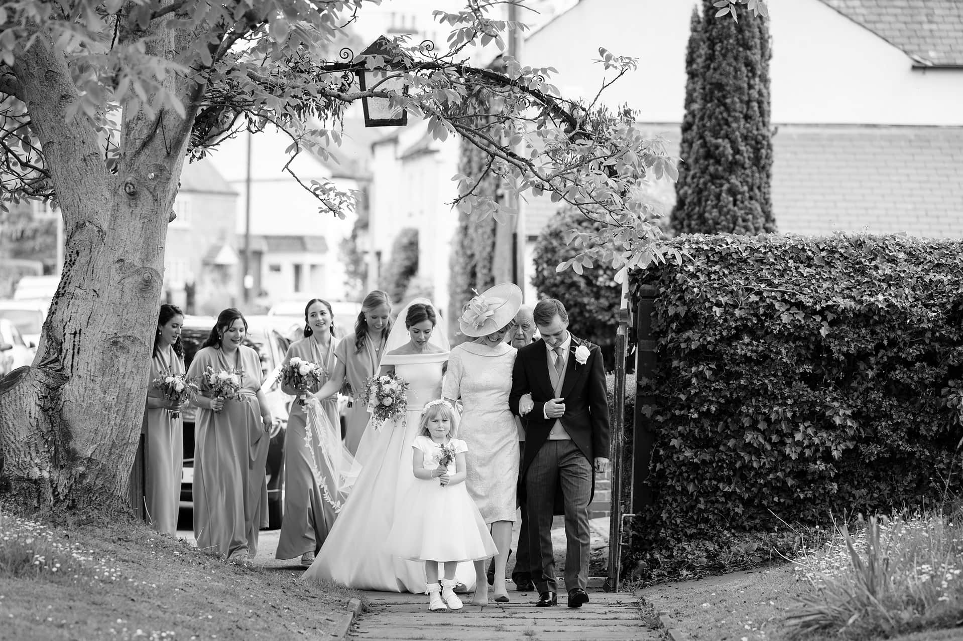 The bride, her family, and bridesmaids walking down St Catharine's church path in Houghton on the Hill