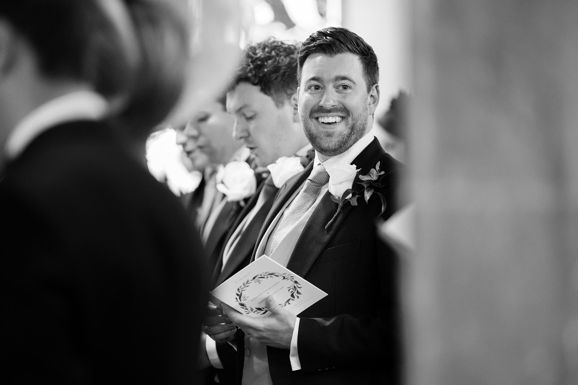Best Man smiling broadly at another wedding guest during a hymn