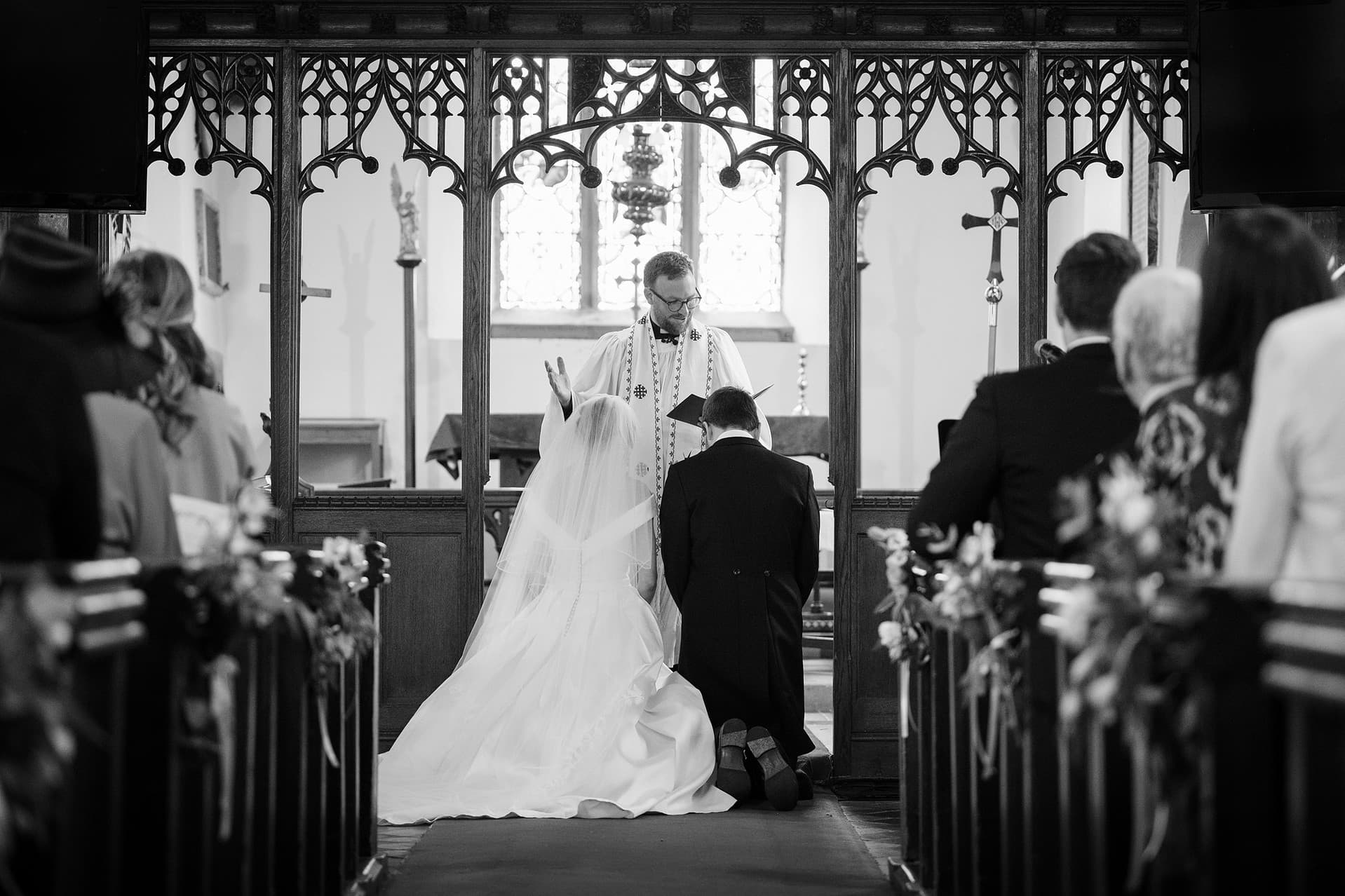 Bride and groom kneeling for the prayers at the end of their ceremony at St Catherine's church in Houghton on the Hill