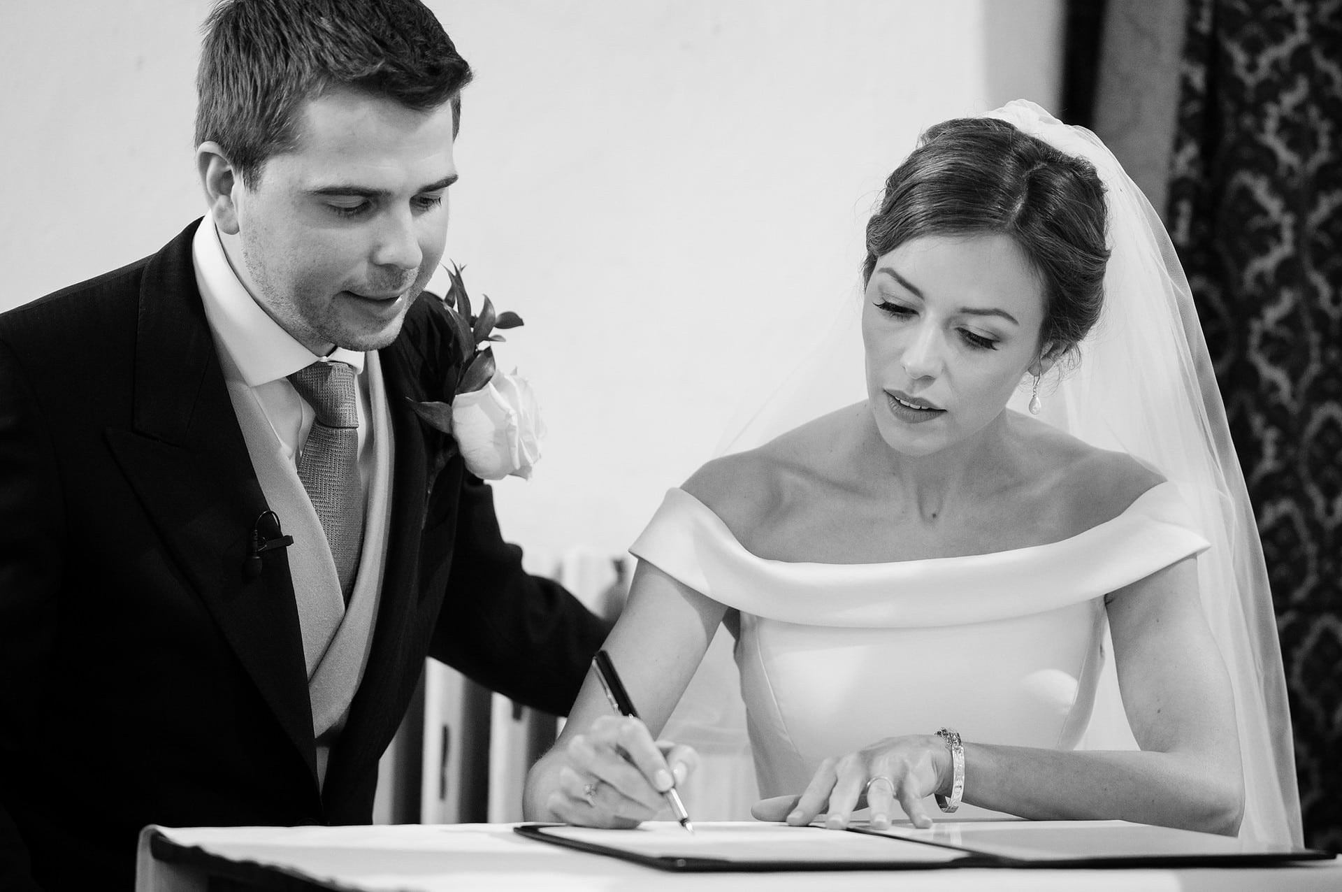 Bride signing the marriage register as the groom looks on at St Catherine's church in Houghton on the Hill