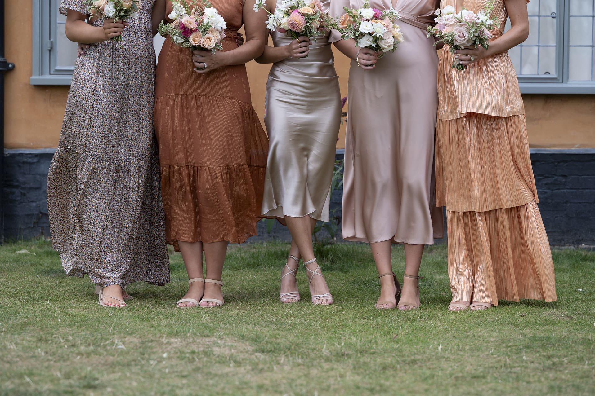 A close up detail photo of bridesmaids wearing mismatched dresses of the same tonal colours of peach, gold, rust, and dusky pink.
