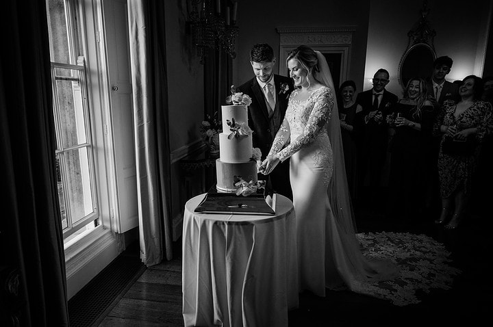 Bride and groom cutting their wedding cake in the Saloon at Kelmarsh Hall