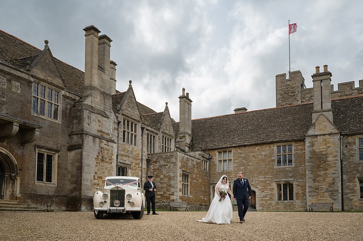 Bride and groom walking next to their wedding car at Rockingham Castle