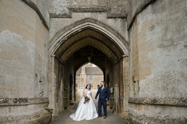 Bride and groom olding hands in front of the two towers at Rockingham Castle