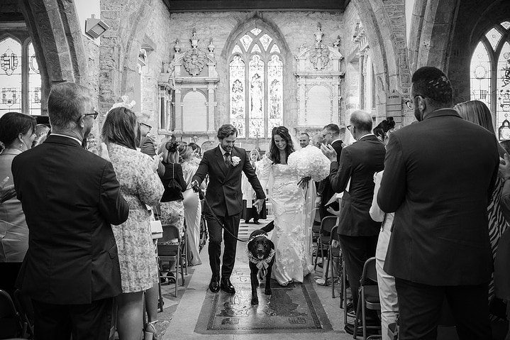 The bride and groom walking down the aisle with their dog at Fawsley church