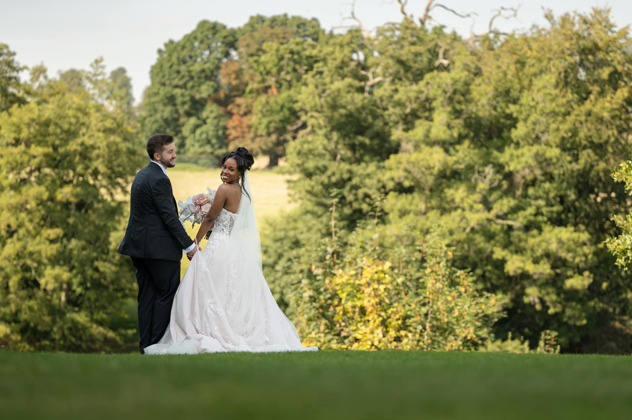 Bride and groom standing in front a countryside backdrop for their photos at Fawsley Hall