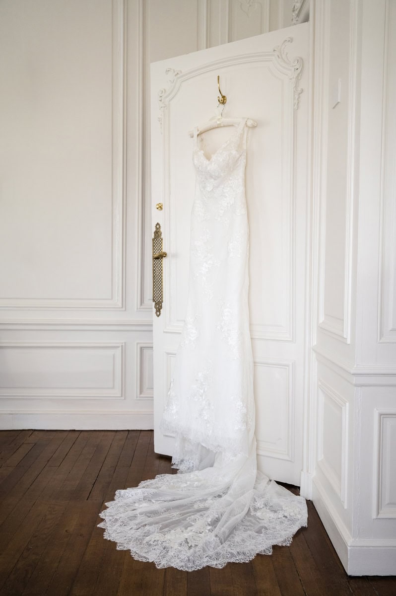 A lace column-style wedding dress hanging on the back of an ornate door with white decorative scroll-like features