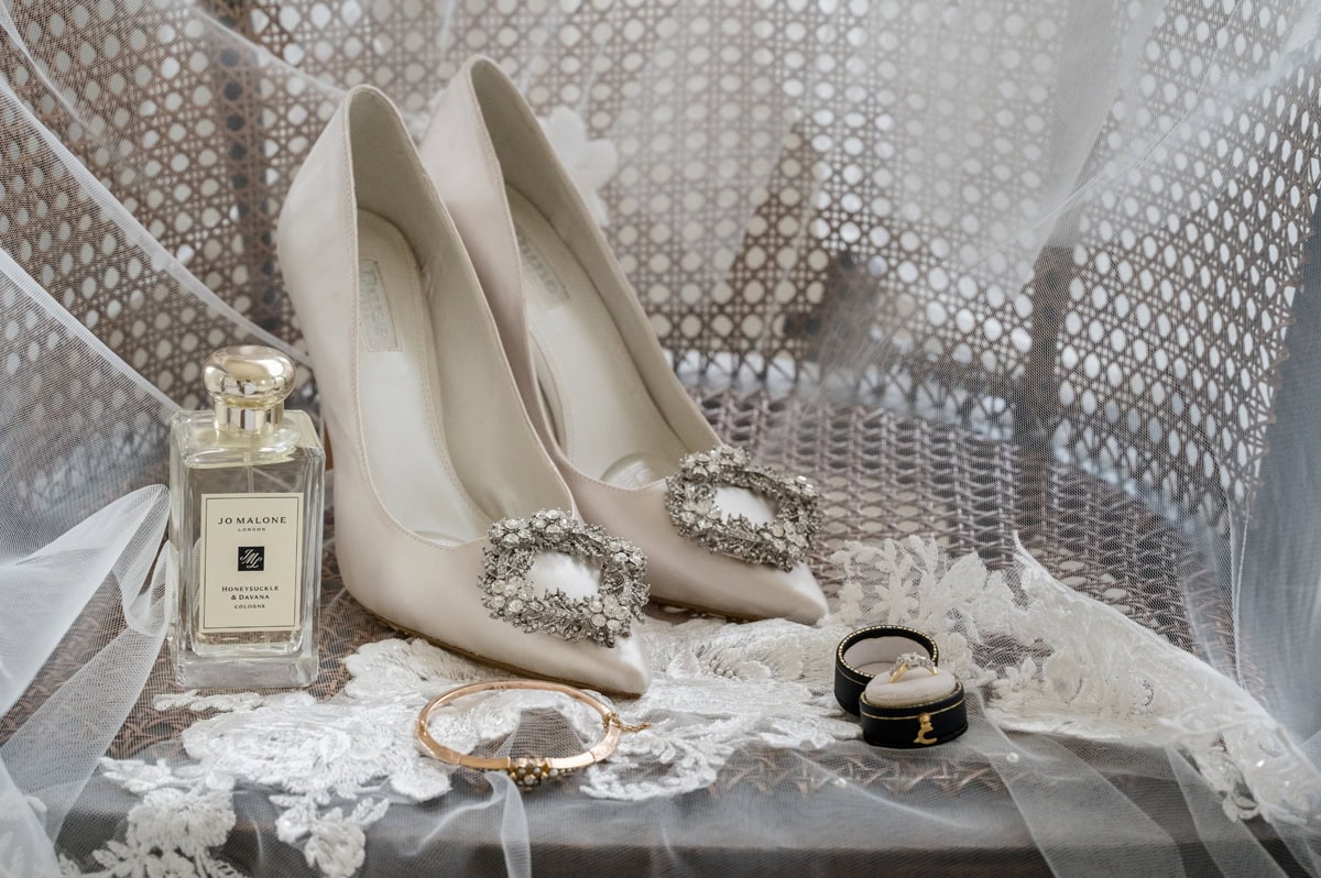 Bride's shoes, perfume, 'something old' ring and bracelet arranged on a woven chair draped with a lace-edged veil