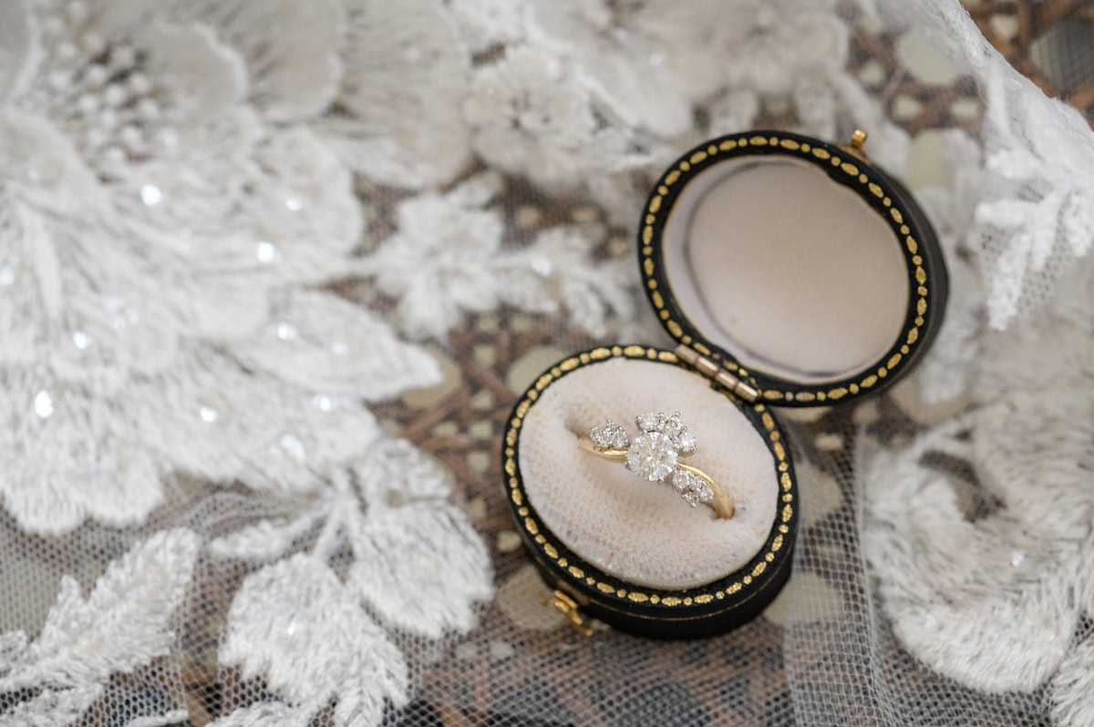 An antique diamond ring in an oval black box with cream lining, on top of a lace veil