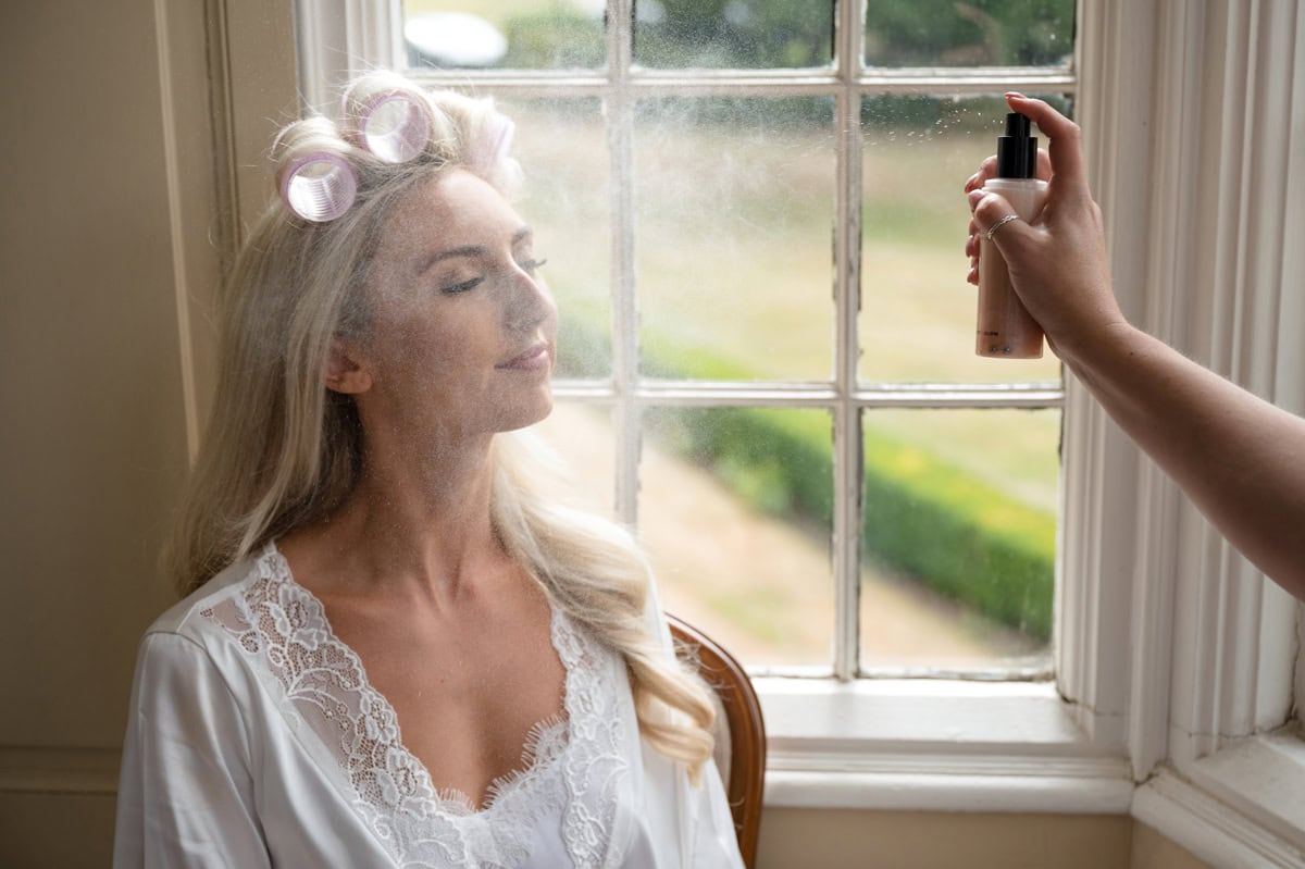 A mist of fixing spray coming out of bottle to set bride's makeup