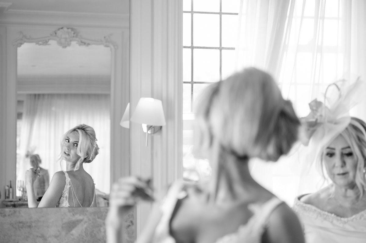 Bride checking out the back of her wedding dress in an ornate mirror on the wall of a grand bathroom